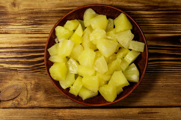 Canned pineapple pieces in ceramic plate on wooden table