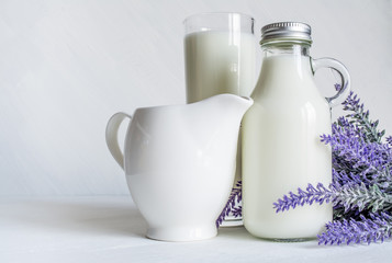 Obraz na płótnie Canvas Vintage glass bottle with milk, next to a beautiful jug and glass of milk and a branch of lavender flowers on a white vintage background