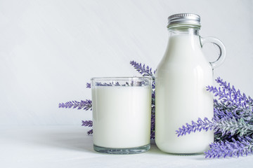 Vintage glass bottle with milk, glass of milk and a branch of lavender flowers on a white vintage background