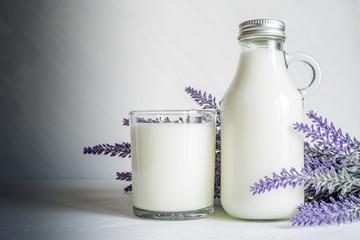 Vintage glass bottle with milk, glass of milk and a branch of lavender flowers on a white vintage background
