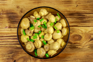 Glass bowl with pickled champignons. Marinated mushrooms on wooden table