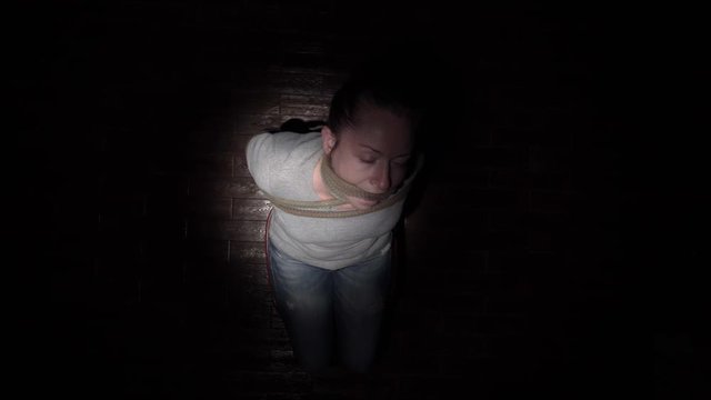 bound prisoner to chair sits in dark room under beam of light. top view.