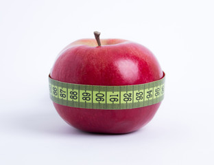 fresh red apple with green measuring tape closeup on white background. healthy vegetarian organic food for diet planning, fitness and lose weight