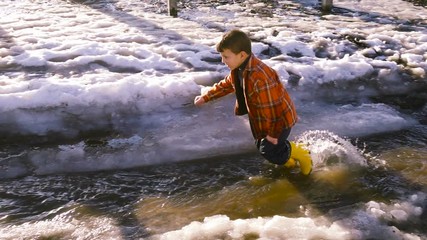 Kid running at the spring creek with melting ice