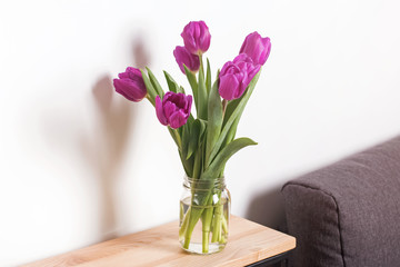Purple tulips in a glass jar standing on the wooden table
