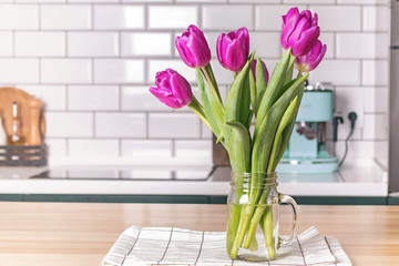 Purple tulips in a glass jar standing on the modern kitchen