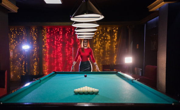 Billiard club. A woman with red hair and nice figure standing by the table. Beautiful lighting