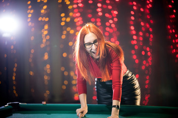 Laughing ginger woman playing billiard in nice architected club