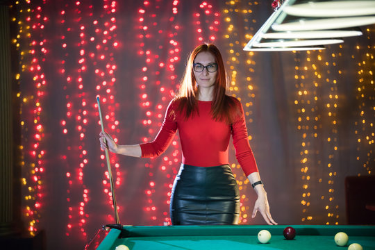 A ginger woman standing in billiard club holding a cue