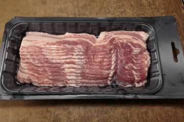 Raw strips of bacon, close-up, in a plastic packing from a supermarket.
