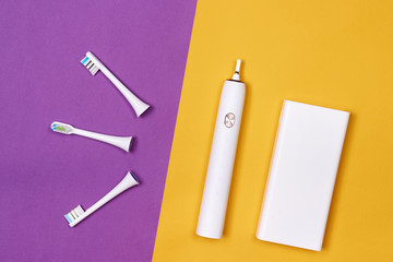 Smart electric toothbrush. Controlled by the application on the smartphone. With power bank. Modern technology for health. Healthy teeth. Dentistry. Purple and yellow paper background