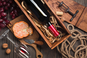 Red wine in a box with a glass, corkscrew and cream cheese on a wooden old table. Top view with space for your greetings.