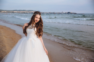 Fototapeta na wymiar Portrait of beautiful bride in stylish wedding dress on ocean beach. Bride with hairstyle and makeup posing on wedding day