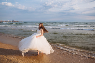 Fototapeta na wymiar Happy beautiful bride in wedding dress whirls and dances on ocean beach