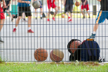 Basketball behind the sports ground fence against blurred training players