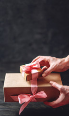 Hands holding Holiday gift boxes Packed in Kraft paper with pink ribbon on dark wooden background.