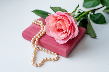 Pearl necklace on rose velvet box and pink one rose. Light background.