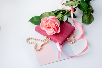 Pearl necklace on rose velvet box and pink one rose with gift card. Light background.