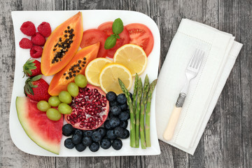 Healthy diet food with fresh fruit and vegetable on a plate with fork and napkin on rustic wood table background. Super foods high in antioxidants, anthocyanins, dietary fibre and vitamins.