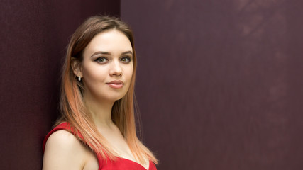 Young woman in a red dress against a dark wall. Caucasian girl in a short red dress with long straight hair.