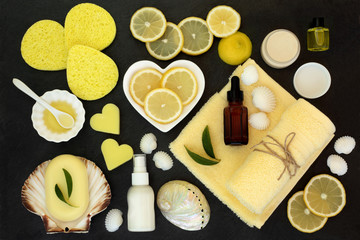 Lemon spa beauty skin care and body care treatment products including  lemons, almond oil, natural soaps, moisturiser, lotion and aromatherapy essential oil. Top view on slate.