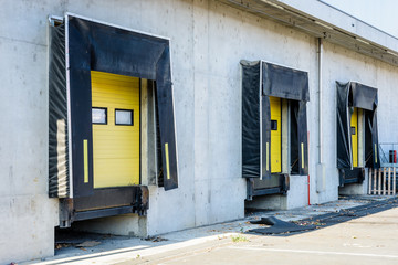 Three truck loading docks with rubber seals in the concrete wall of a warehouse in the suburbs of Paris, France, with a closed yellow roller shutter door.