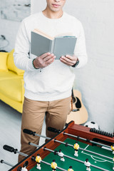 partial view of man reading book while standing by football table