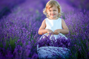 Cute curly young girl standing on a lavender field in white dress and hat with cute face and nice hair with lavender bouquet and smiling.