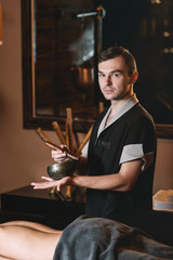 Specialist holding in hands Brass Hammer Singing Bowl. beautiful woman spending time at modern spa cabinet relaxing. Soft yellow light