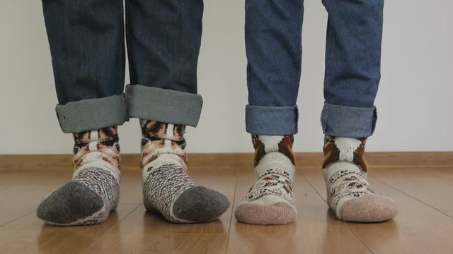 Close-up of the legs of a man and a woman in warm woolen socks are standing on the wooden floor in the room and trampling