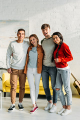 smiling multiethnic friends standing together in living room and looking at camera