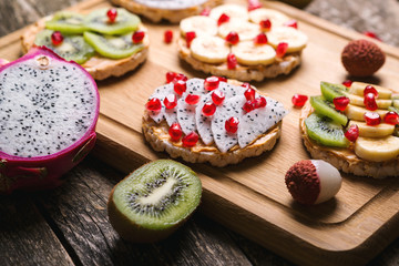 Healthy organic and vegan breakfast. Mini sandwiches with peanut butter and tropical fruits. Fruit summer snack. Sandwiches with dragonfruit, banana, kiwi and pomegranate on wooden table. Fruits diet.