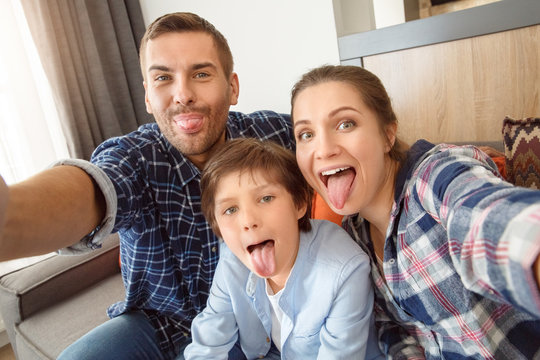 Family at home sitting on couch in living room together taking selfie pictures tongue out playful