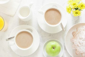 Breakfast on white background. Tea or coffee with milk, apple pie, apple, orange juice and yellow flowers