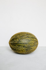 A green melon lies on a light background