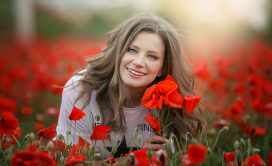 Naklejka premium Beautiful happy smiling teen girl portrait with red flowers on head enjoying in poppies field nature background. Makeup and curly hair style. Lifestyle.