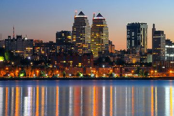 The lights of the Beautiful tall buildings, skyscrapers,  towers are reflected in the Dnieper River at sunset in the evening.  Dnipro city, Dnipropetrovsk, Ukraine