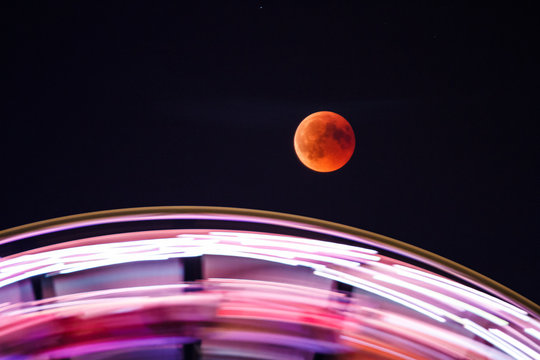 Mondfinsternis &uuml;ber einem sich drehenden Riesenrad
