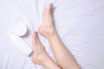 Female legs feet heel foot white jar cream in white bed, top view