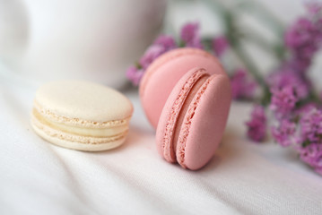 Pink and white cream macarons decorated with small purple flowers on white cloth