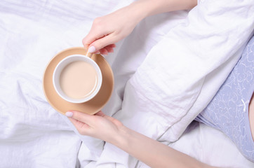 Fototapeta na wymiar Woman holding cup of coffee in the white linens bed, top view