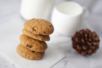 Stack of tasty oatmeal raisin cookies on marble table with pinecone and white milk mug       