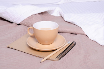 Fototapeta na wymiar Cup of coffee witrh saucer notepad pencil on a white brown bed home design