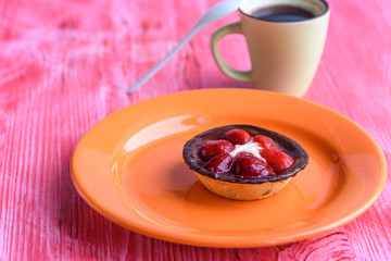 A cupcake with a strawberry, next to coffee in a cup, photographed on a wooden background.