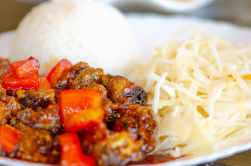 Chinese food, rice with seafood and red peppers in soya sauce and vegetables, cabbage and carrots in a white plate, close up