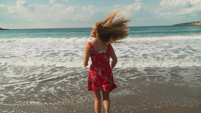 Guy in black pants and a white T-shirt and a girlfriend in a red dress with flowers running into the sea or ocean. Slow motion.