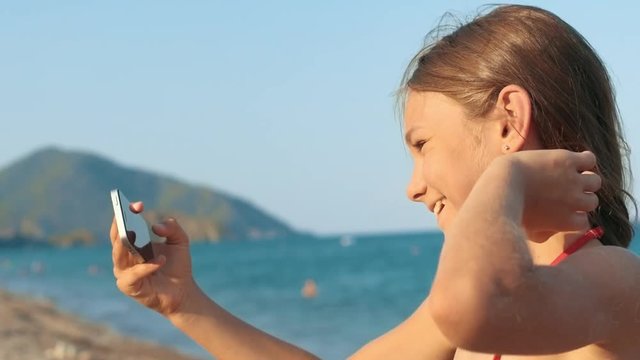 Little girl posing in front of phone camera making selfie at seashore