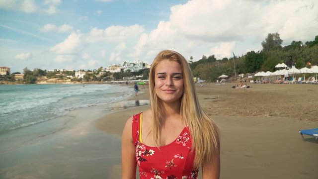 Portrait of young woman with blond hair standing at the beach close up. Lonely girl spends time near the sea. Leisure of young lady. Image zooms