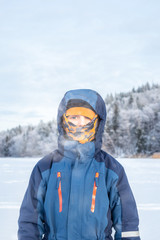 Fototapeta na wymiar Arctic outdoor winter portrait of a child boy in winter clothing with balaclava against frozen landscape background.