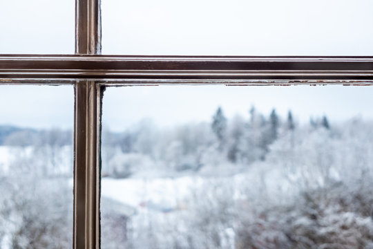 Freezing white winter landscape seen through a window glass with wooden frame.